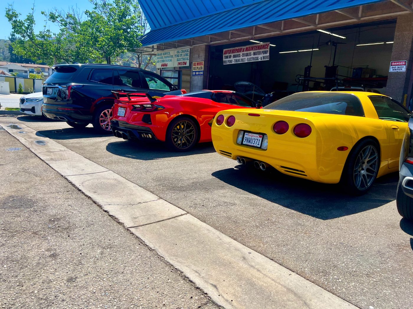 A lineup of Corvettes and SUVs waiting for service outside All Model Repair in Glendale